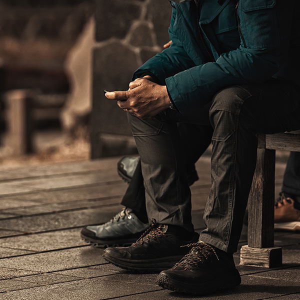 Two hikers sitting on a bench; man using a smartphone.